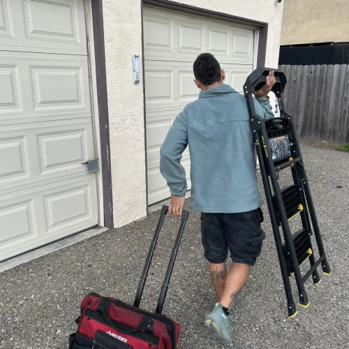 carlos garage door technician carrying a stair to service a garage door in huntington beach
